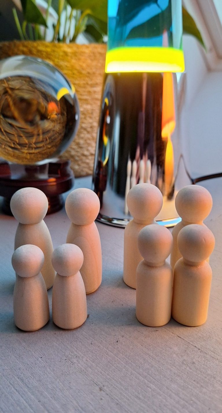 Sechs Holzfiguren stehen in zwei Gruppen auf einem Tisch, umgeben von sanftem Licht.