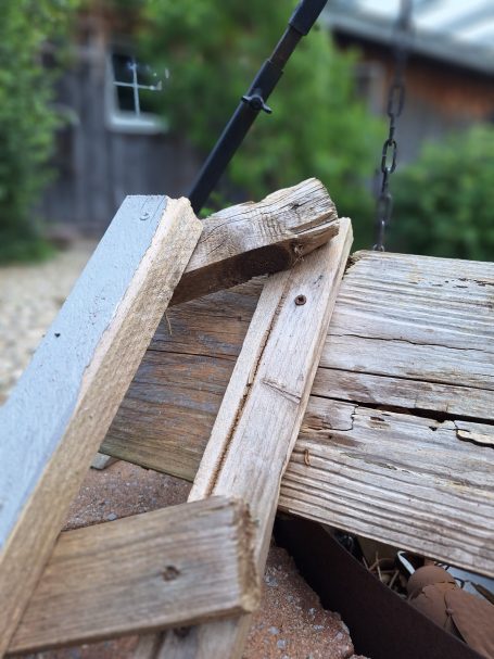 Holzkonstruktion mit mehreren Brettern, die teilweise übereinanderliegen, in einem Garten.